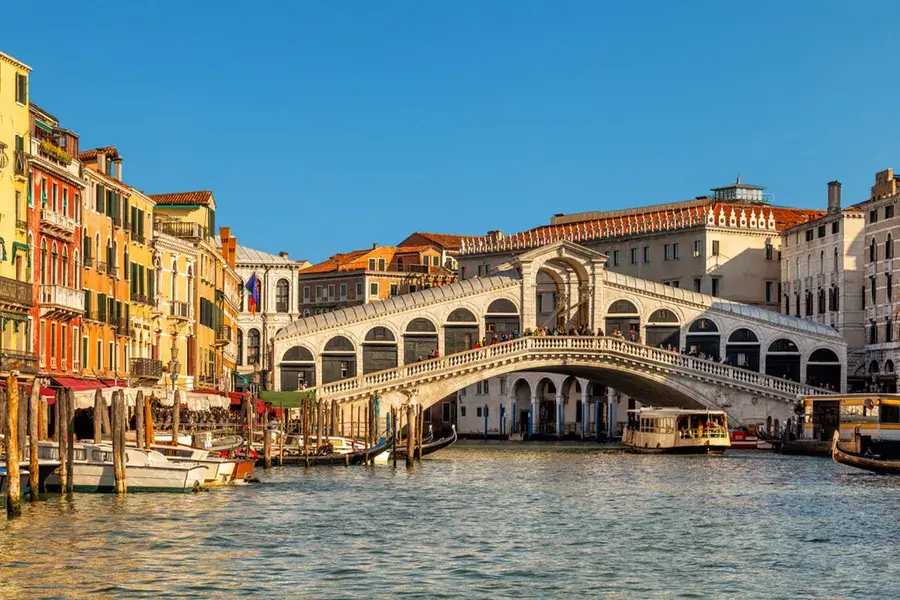 Il Ponte di Rialto sul Canal Grande di Venezia, edifici vivaci, barche, cielo azzurro e limpido.