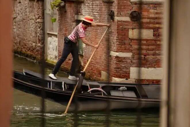 Un gondoliere con cappello di paglia e strisce guida la gondola attraverso uno stretto canale.