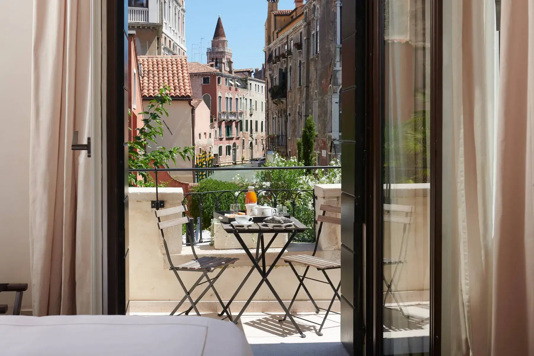 Un balcone con tavolo e sedie si affaccia su un canale. La colazione è apparecchiata sul tavolo.