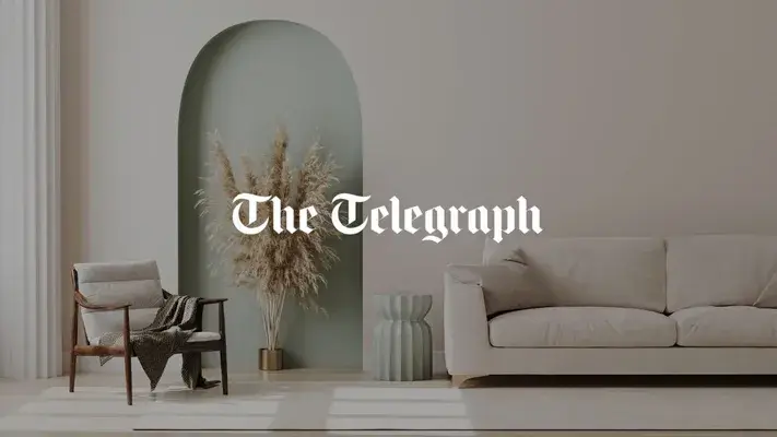 Stanza minimalista: divano bianco, sedia di legno, erba della pampa in un vaso vicino alla parete ad arco; logo del Telegraph.