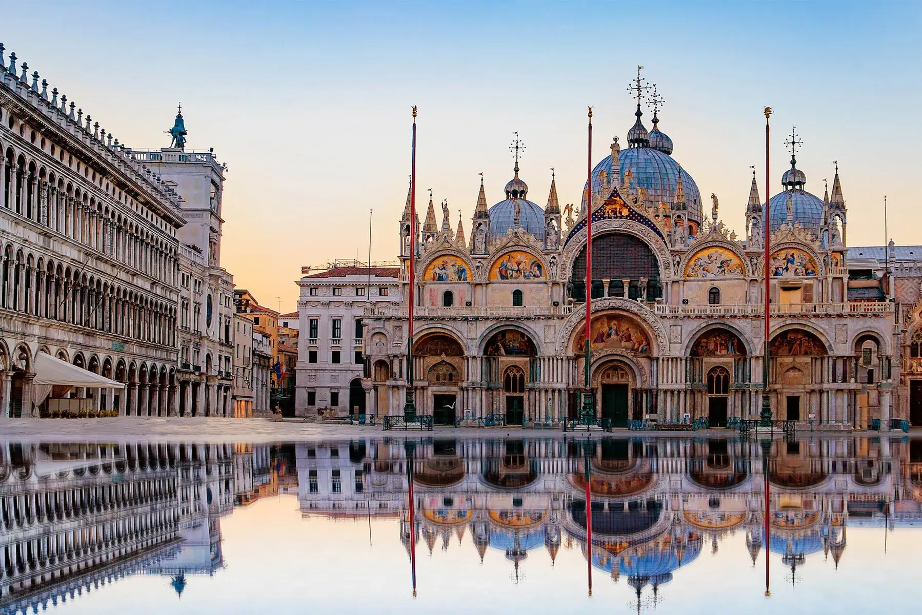 La Basilica di San Marco a Venezia si riflette nell'acqua di Piazza San Marco al tramonto.