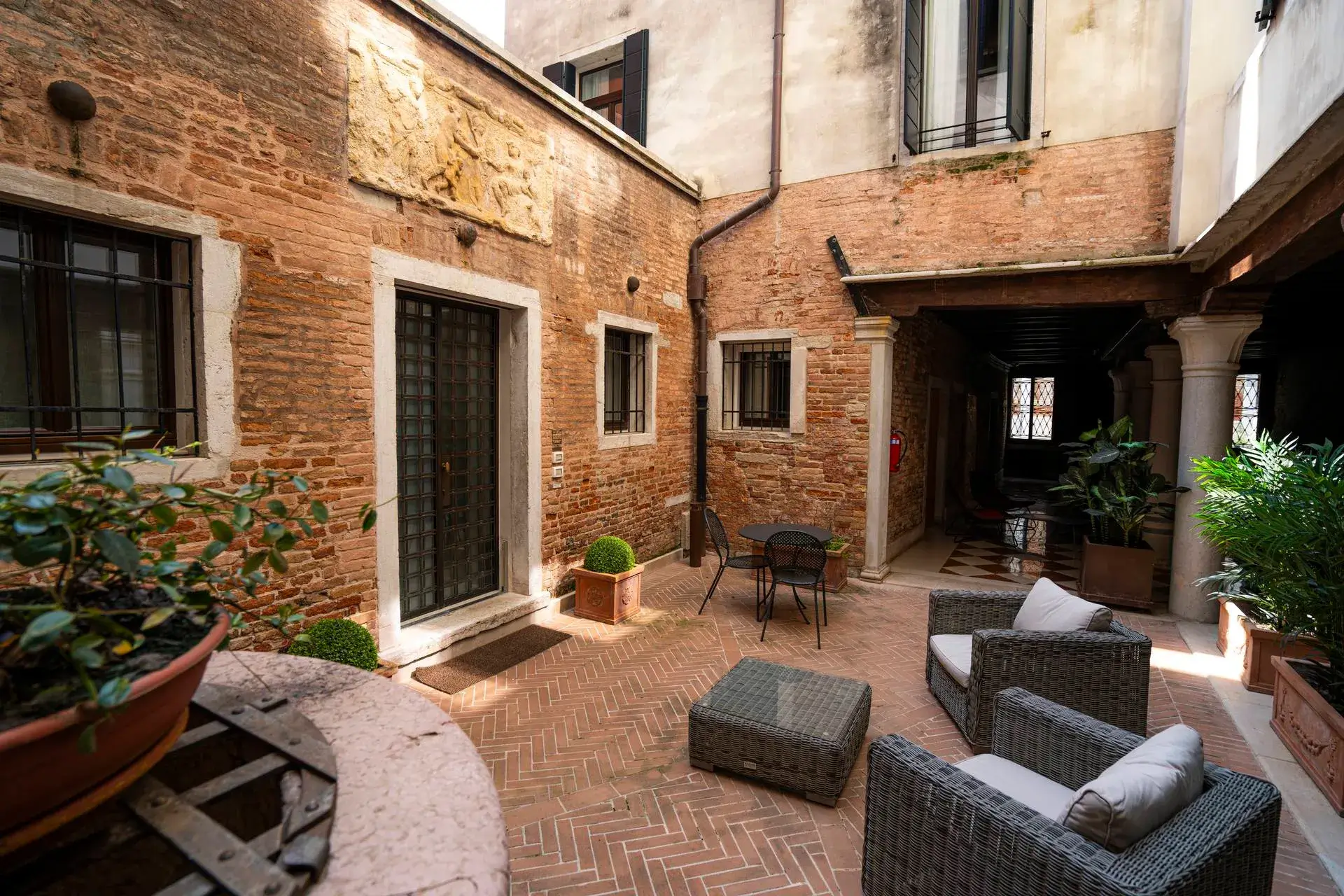 Cortile con muro in mattoni: mobili in vimini, piante, tavolo rotondo e sedie vicino alla porta.