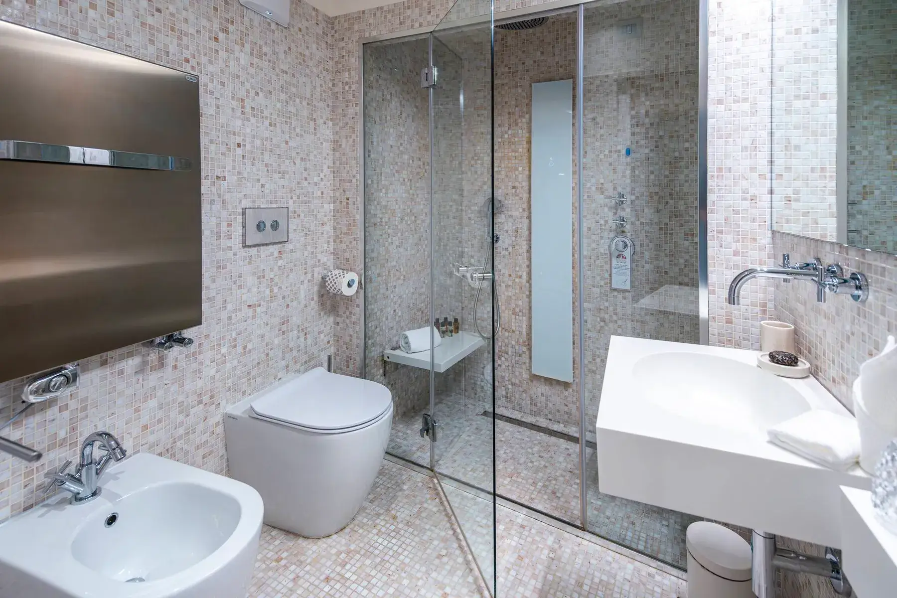 Bagno moderno: doccia in vetro, WC e bidet bianchi, lavabo a muro, pareti piastrellate a mosaico.