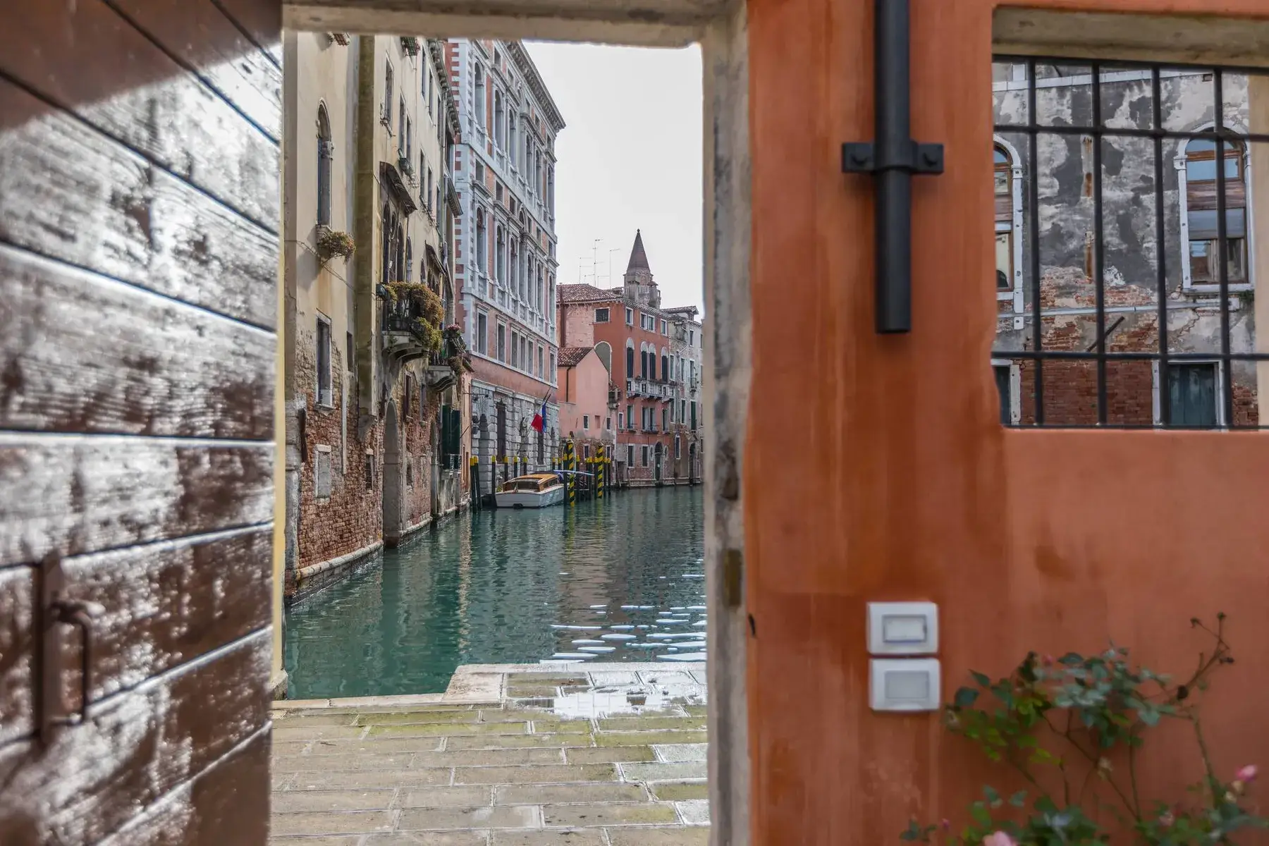 Vista attraverso una porta di un canale veneziano con edifici colorati e una piccola barca.