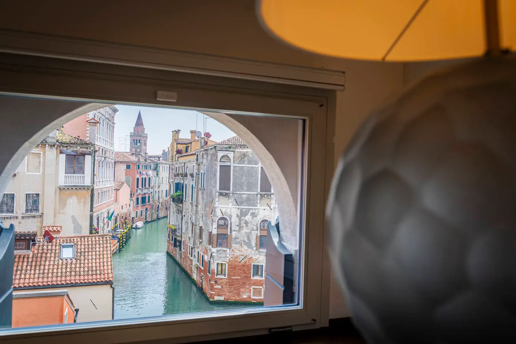 Vista del canale veneziano da una finestra, Palazzo Morosini degli Spezieri e lampada sfocata in primo piano.