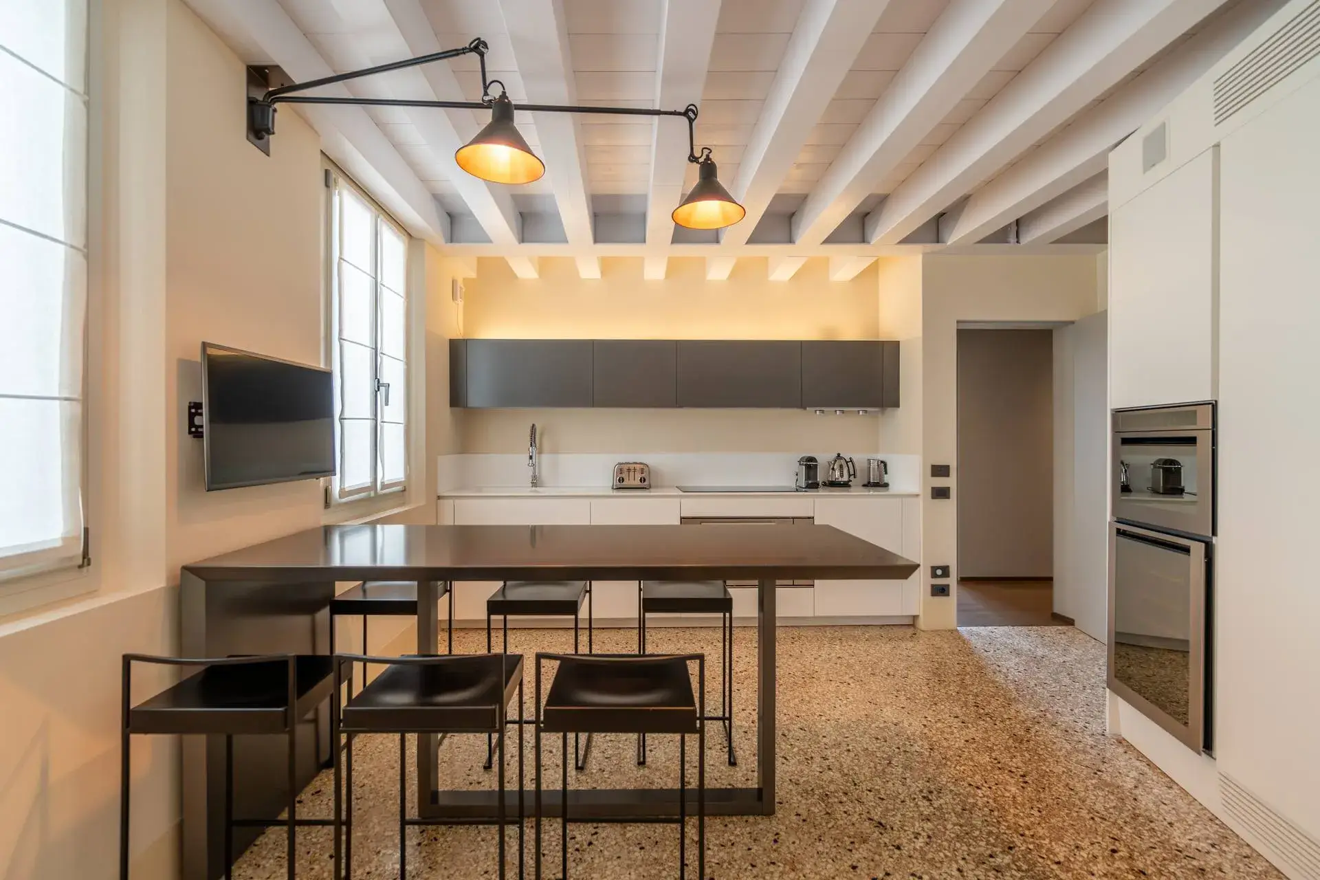 Elegant kitchen: large island, black chairs, hanging lamps, minimalist white cabinets.