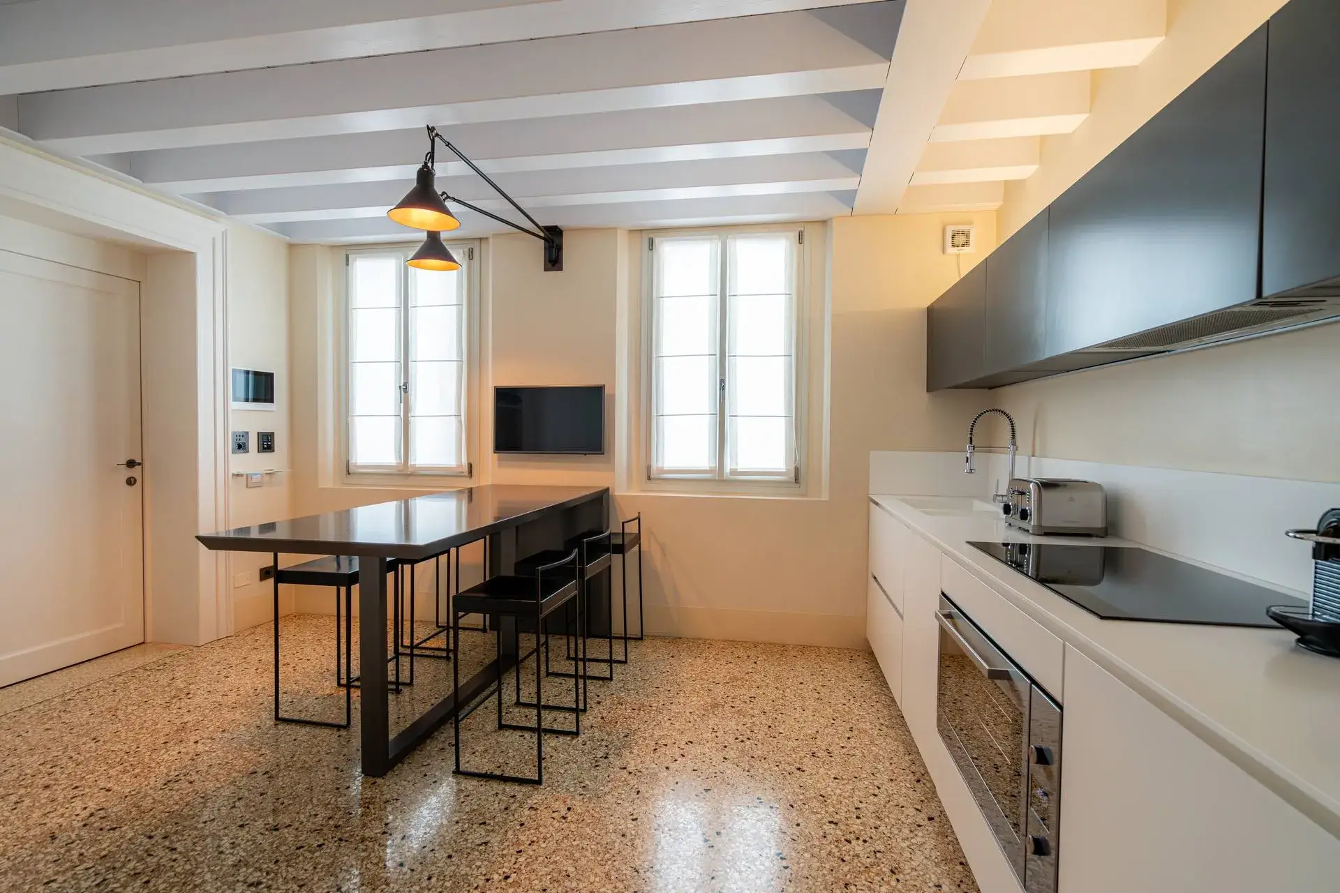 Modern kitchen: white cabinets, black table, large windows, stylish appliances, lights from the ceiling.