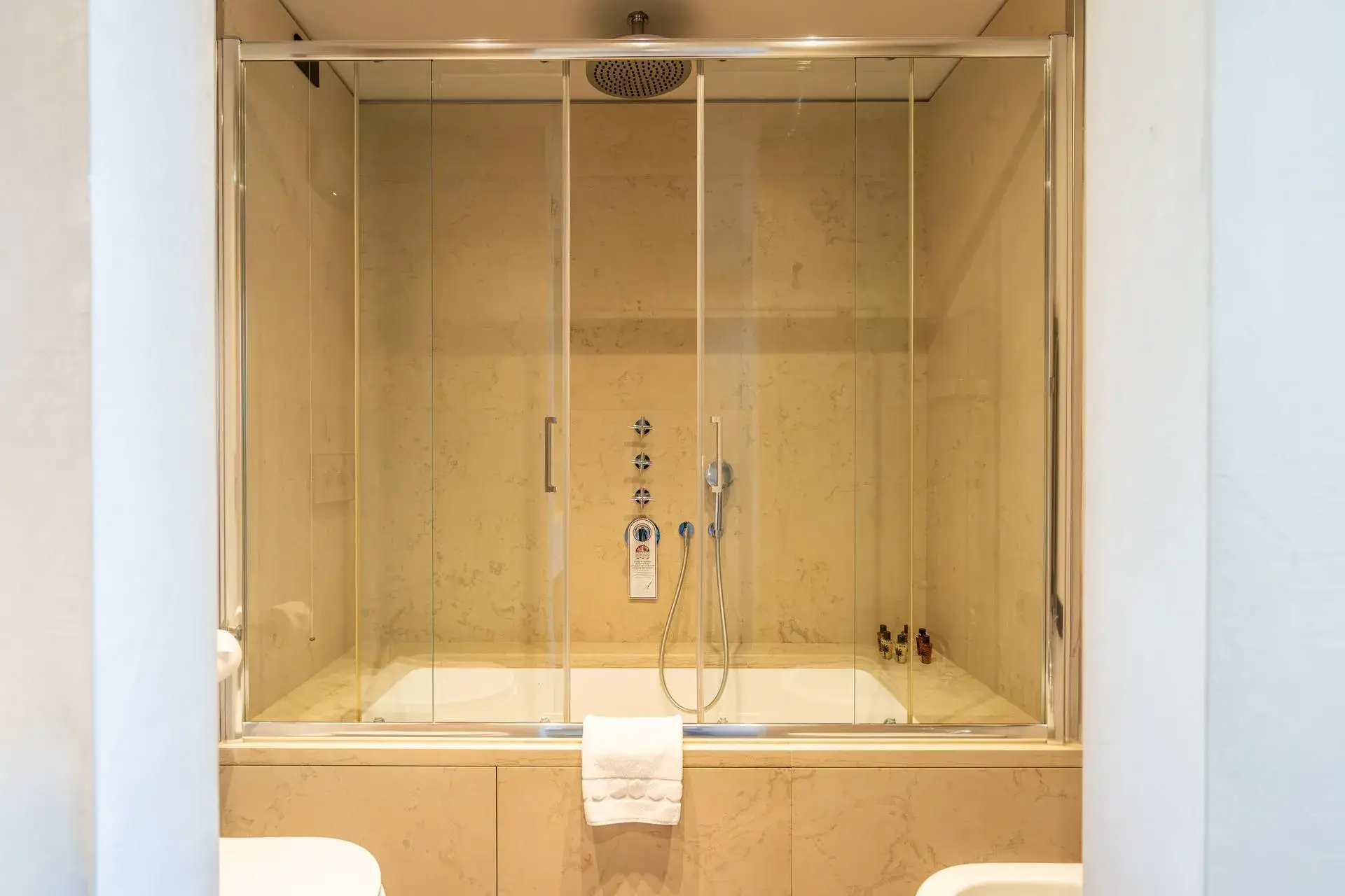 Modern bathroom with glass tub/shower, beige tiles and a carefully hung towel.