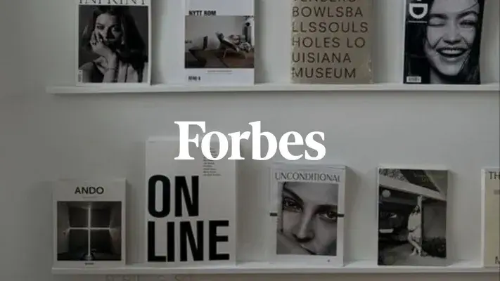 Scaffale con libri e riviste, numero di Forbes visibile di fronte.