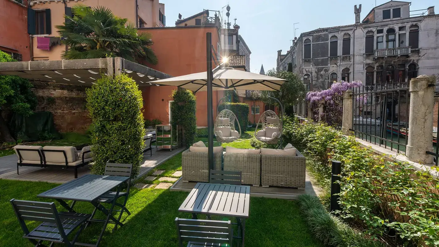 Un accogliente giardino con posti a sedere nel patio, sedie, una tettoia e vista sul verde e sul canale.