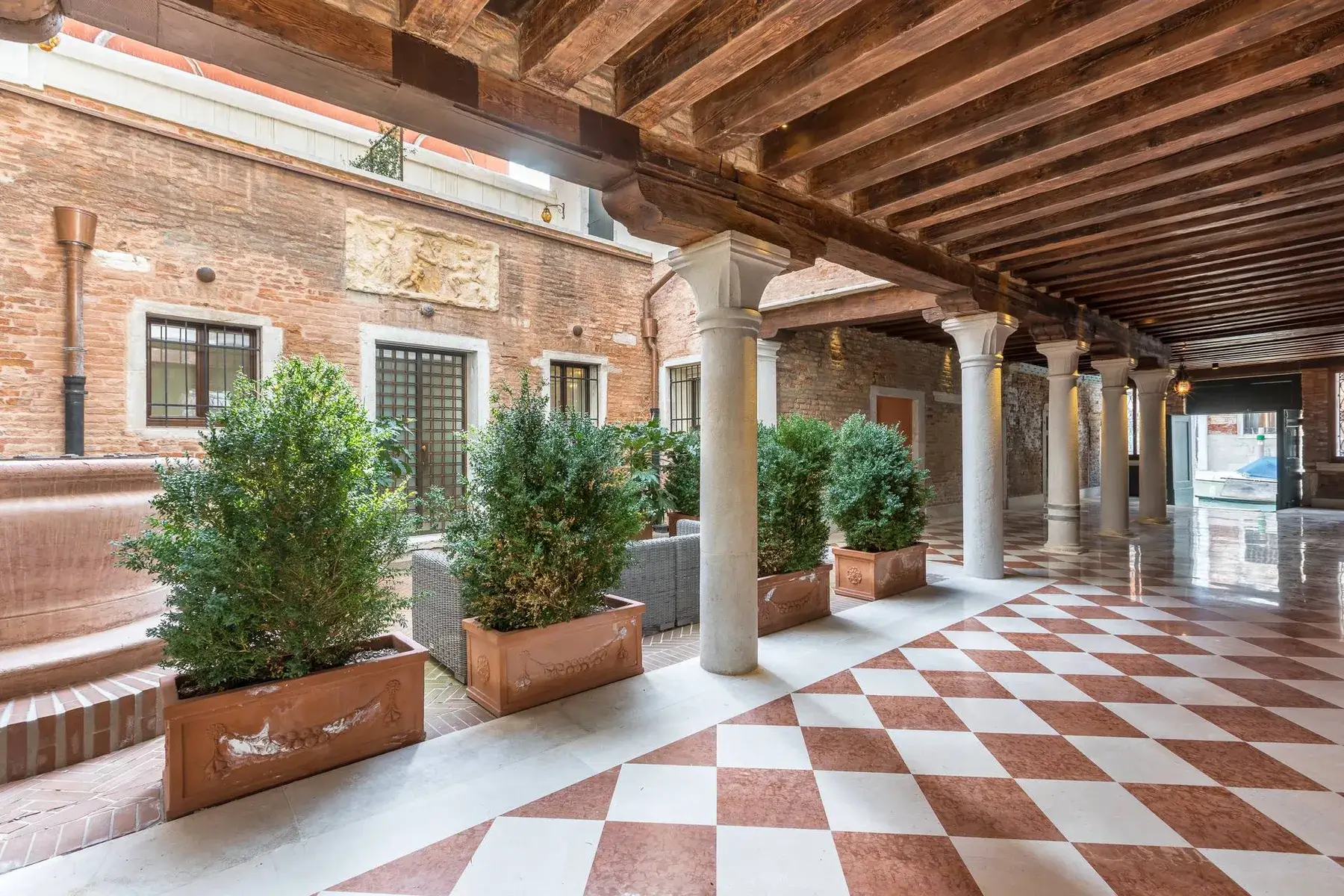 A historic walkway with columns, plants, and a checkered floor.