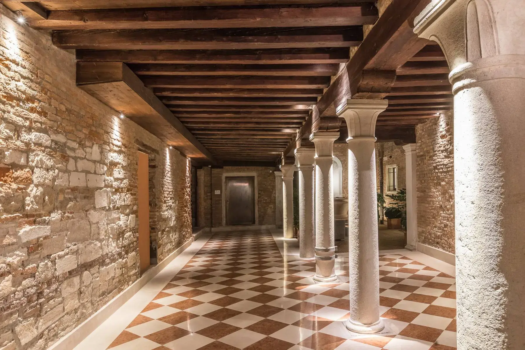 Elegante sala: colonne in pietra, pareti in mattoni, soffitto in legno, piastrelle a scacchi e luci calde.