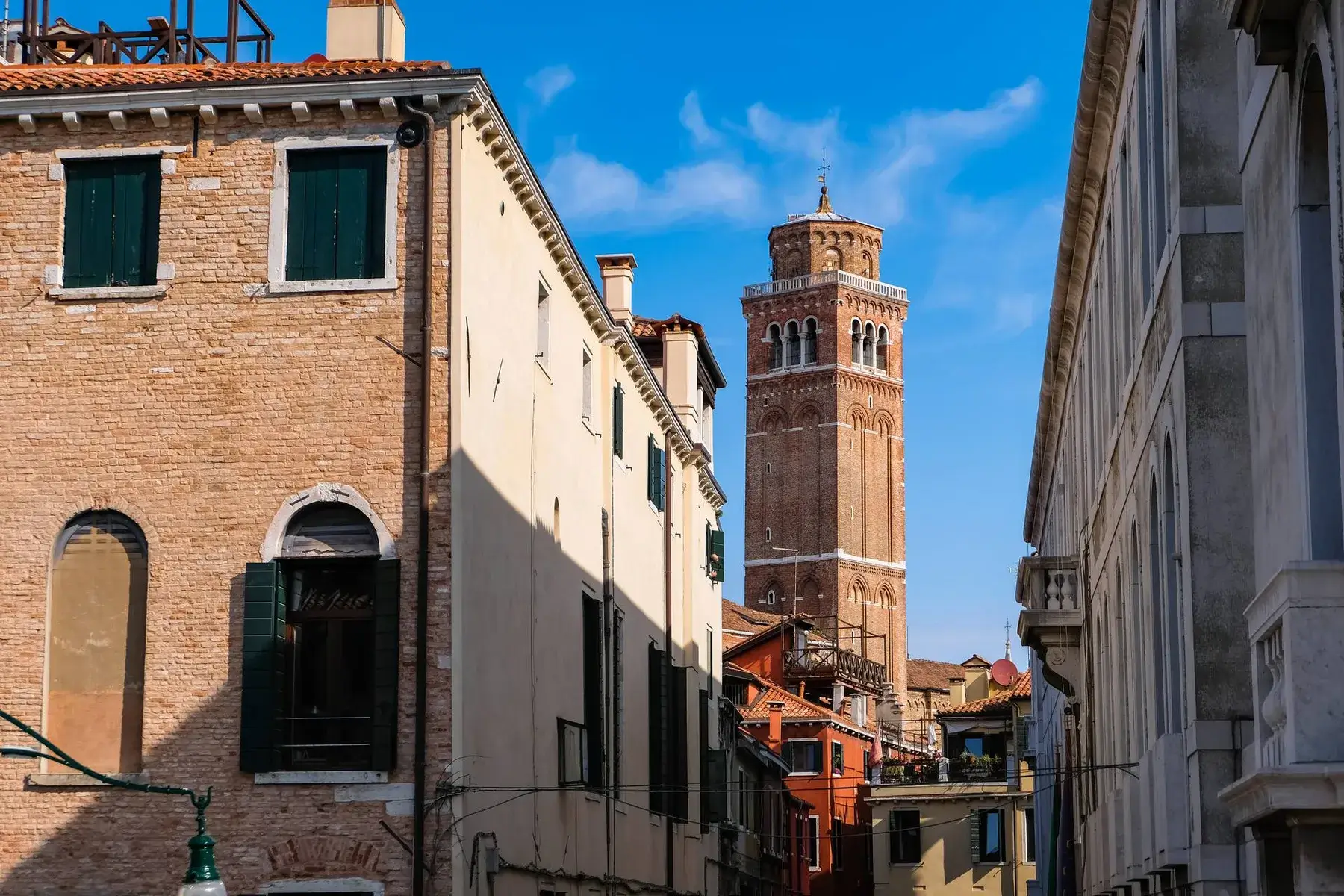 Un'alta torre dell'orologio in mattoni si erge sopra gli Palazzo Morosini degli Spezieri, contro un cielo azzurro e limpido.