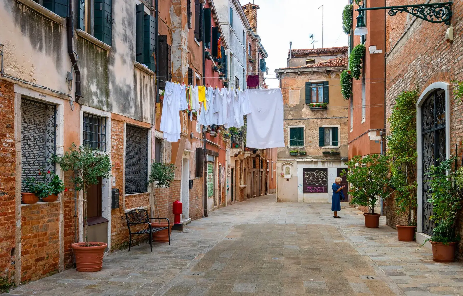 Una strada stretta con i panni stesi e una persona al telefono sulla destra.