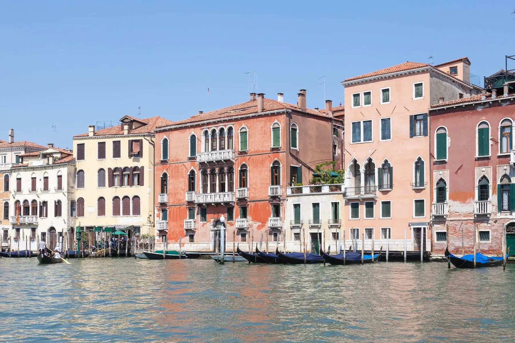 I canali di Venezia con gli edifici colorati e le gondole sotto un cielo terso e azzurro.