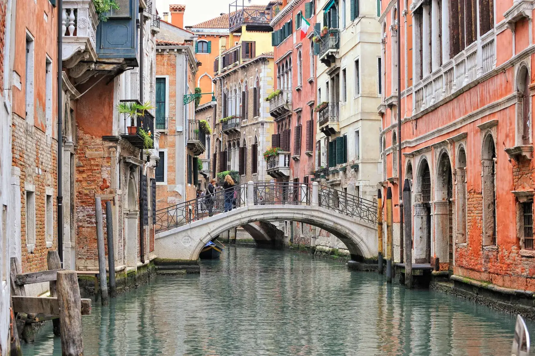 Un canale veneziano con edifici colorati, un ponte ad arco e persone che passeggiano lungo di esso.