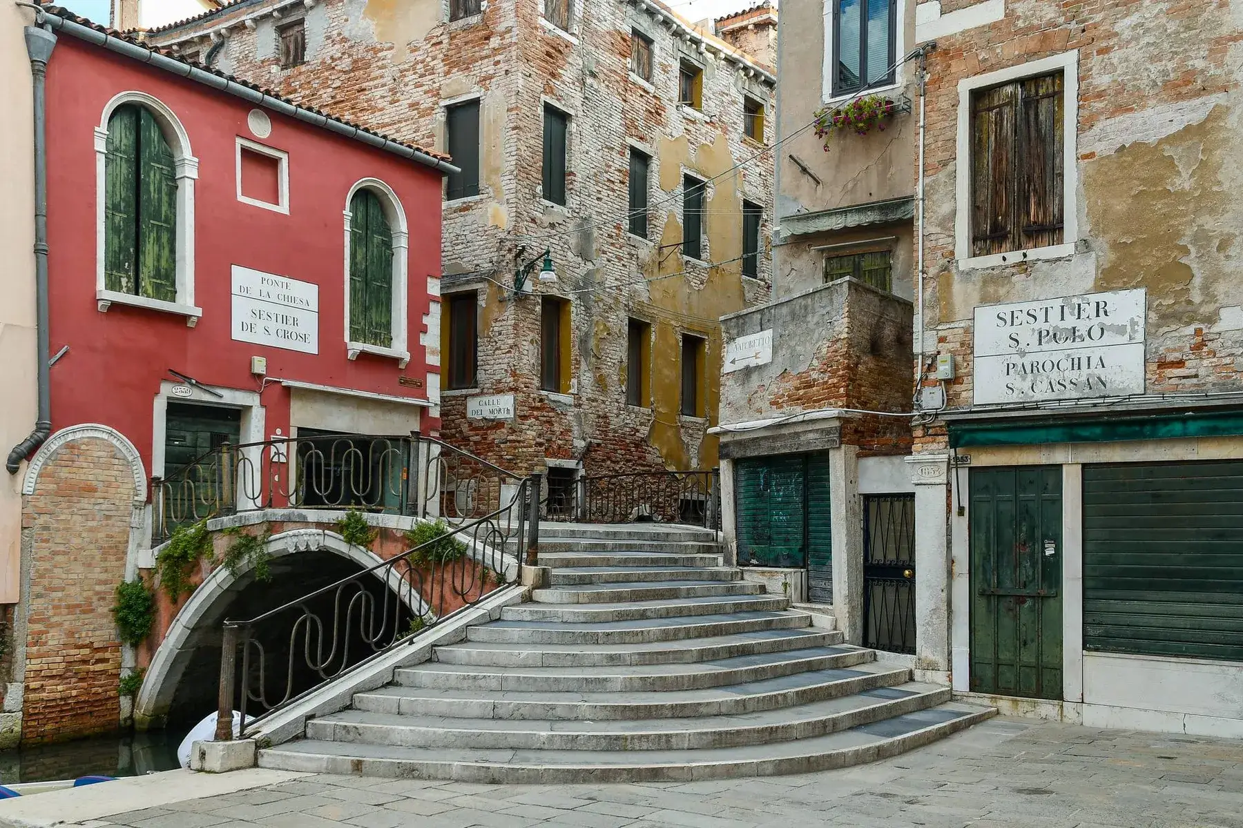 Pittoresca strada di Venezia: ponte in pietra, scale e colorati edifici consumati dal tempo.