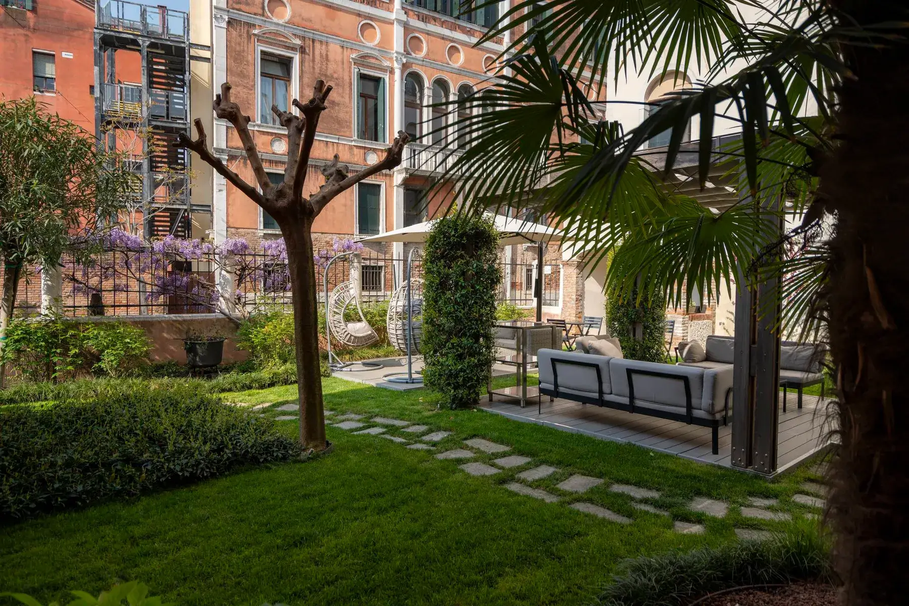 Oasi giardino con posti a sedere, alberi e un edificio sullo sfondo.