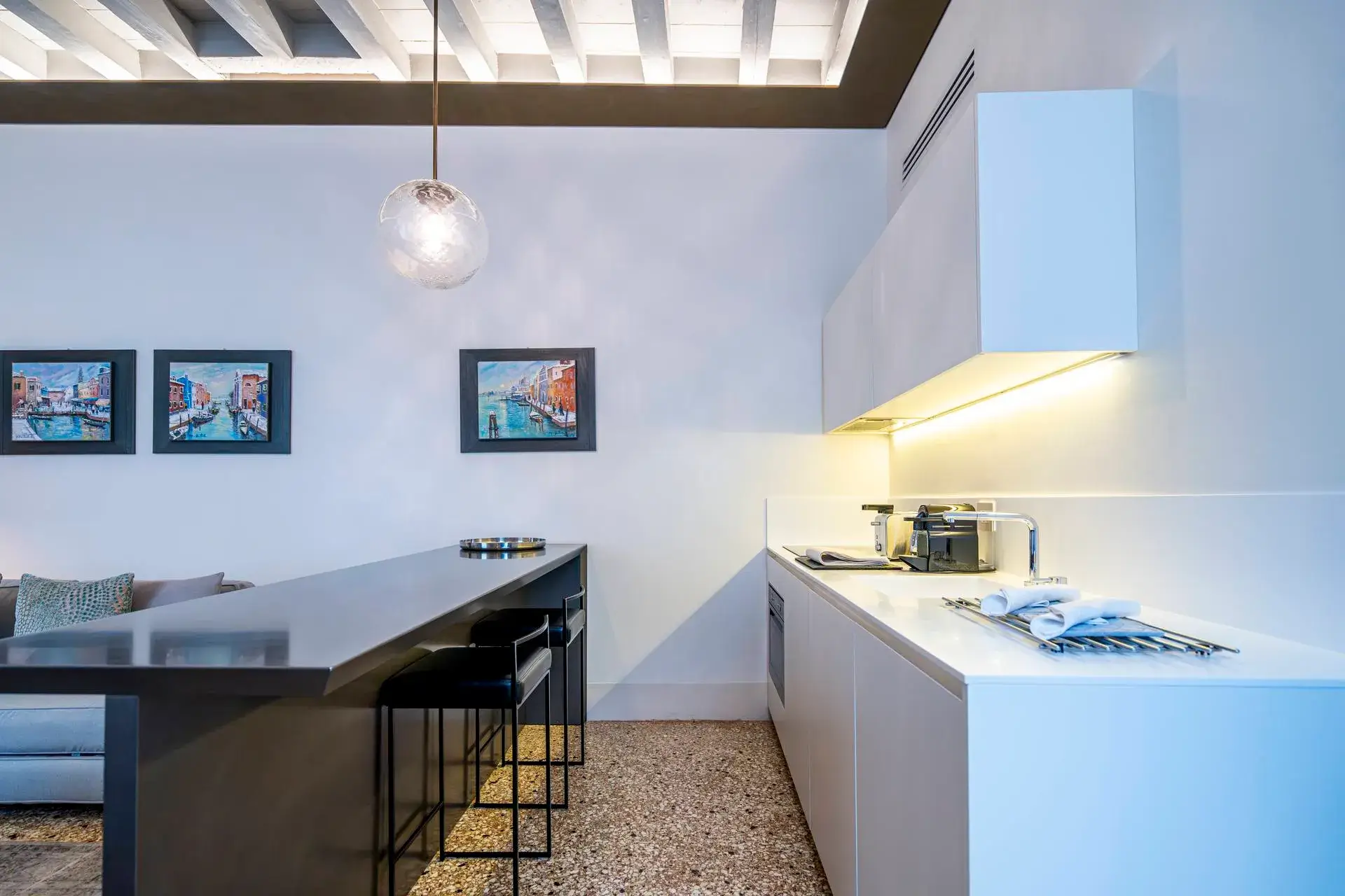 Modern kitchen: white cabinets, black island with stools, and wall art.