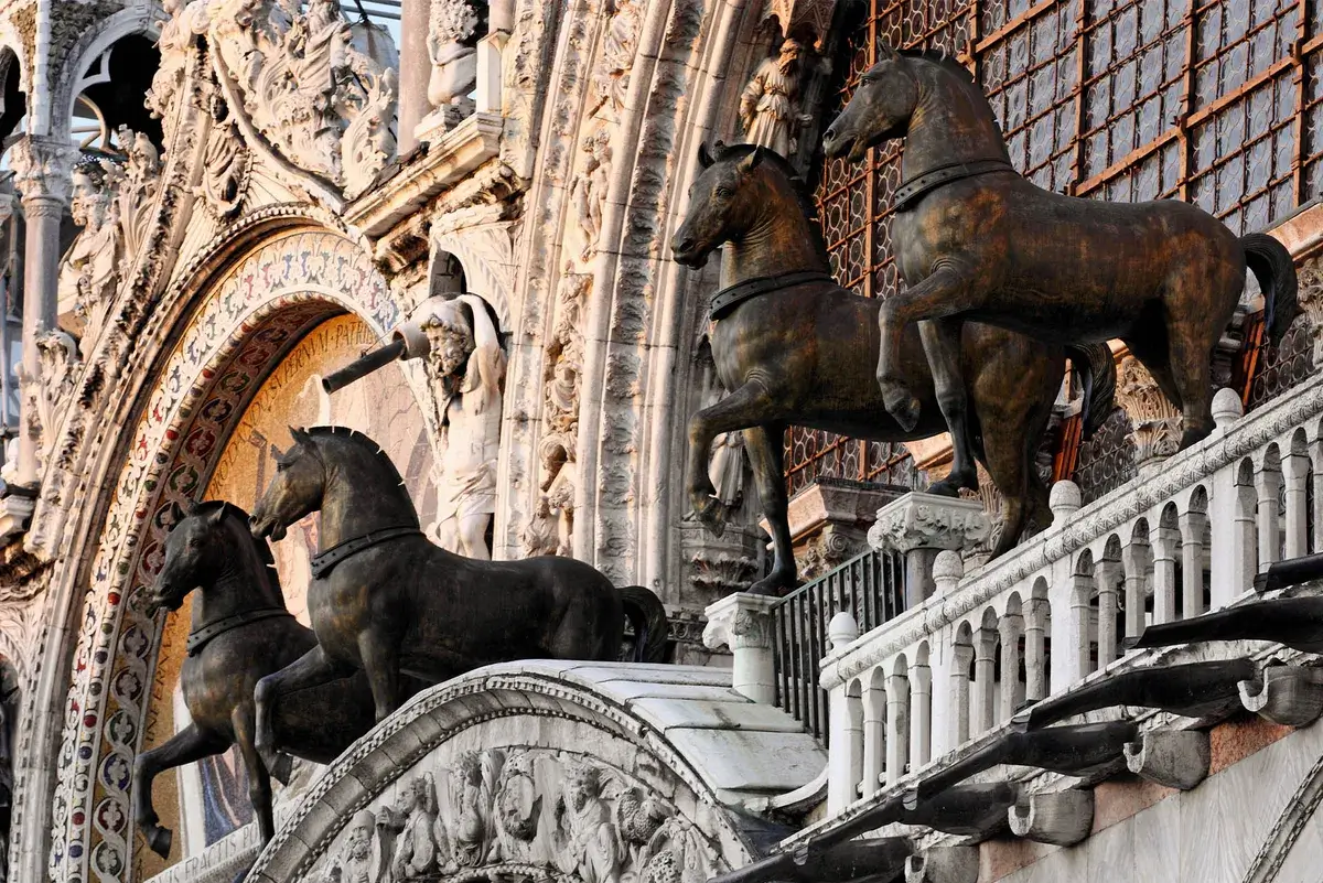 Quattro statue di cavalli in bronzo ornano il balcone decorato ad archi di un edificio storico.