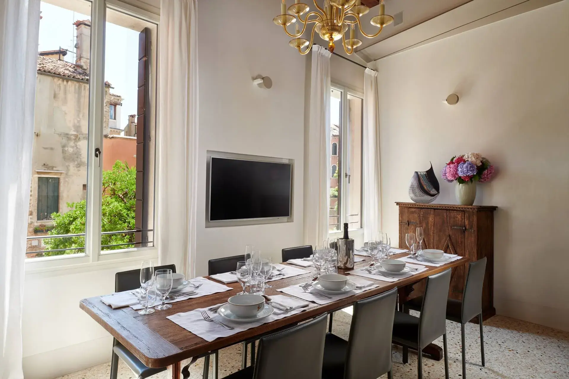 Sala da pranzo: tavolo in legno per sei, lampadario, grandi finestre con vista sull'edificio storico.